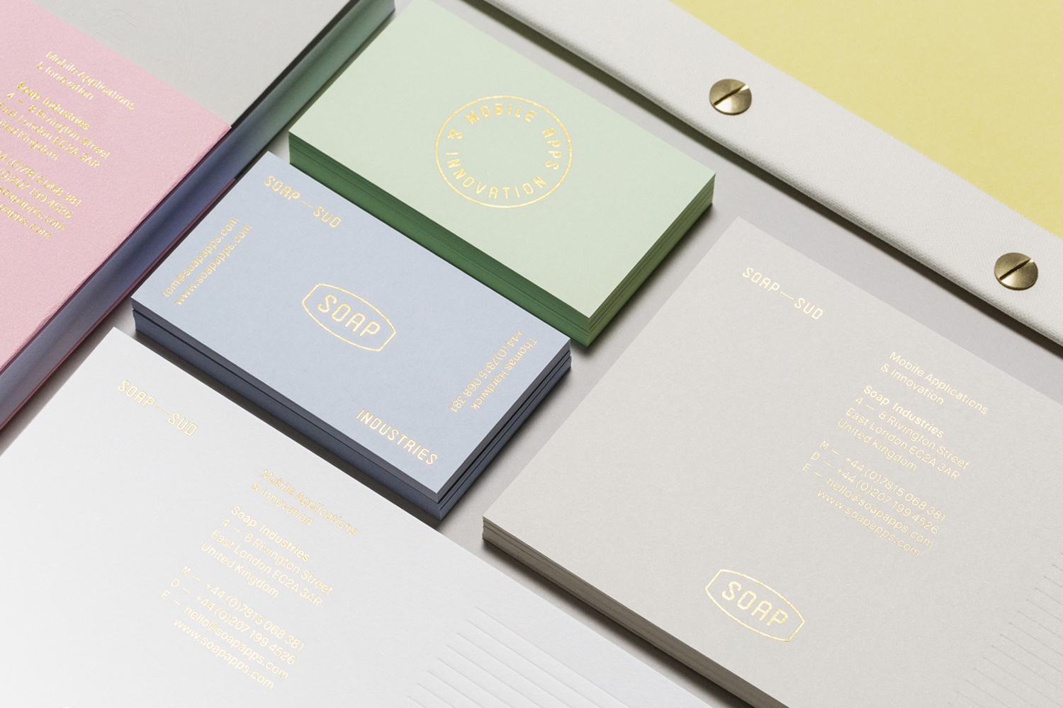 Overhead view of stacked pastel business cards and stationery with gold foil stamped logos for Soap Industries.