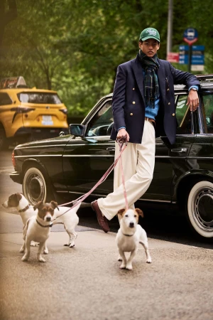 Model leaning against a vintage car holding three dogs on leashes on a city street