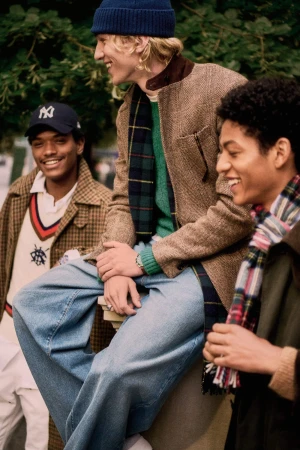 Three young men in autumn outerwear and caps smiling outdoors against a background of green foliage