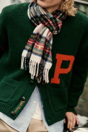 A man wearing a green cardigan with a red letter P and a plaid fringed scarf for Polo Ralph Lauren fall 2025 campaign.