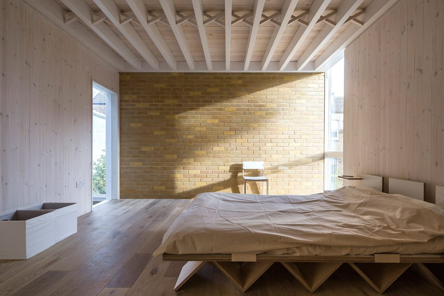 Minimalist modern bedroom interior featuring light wood paneling, exposed ceiling beams, a yellow brick accent wall, and a low platform bed.