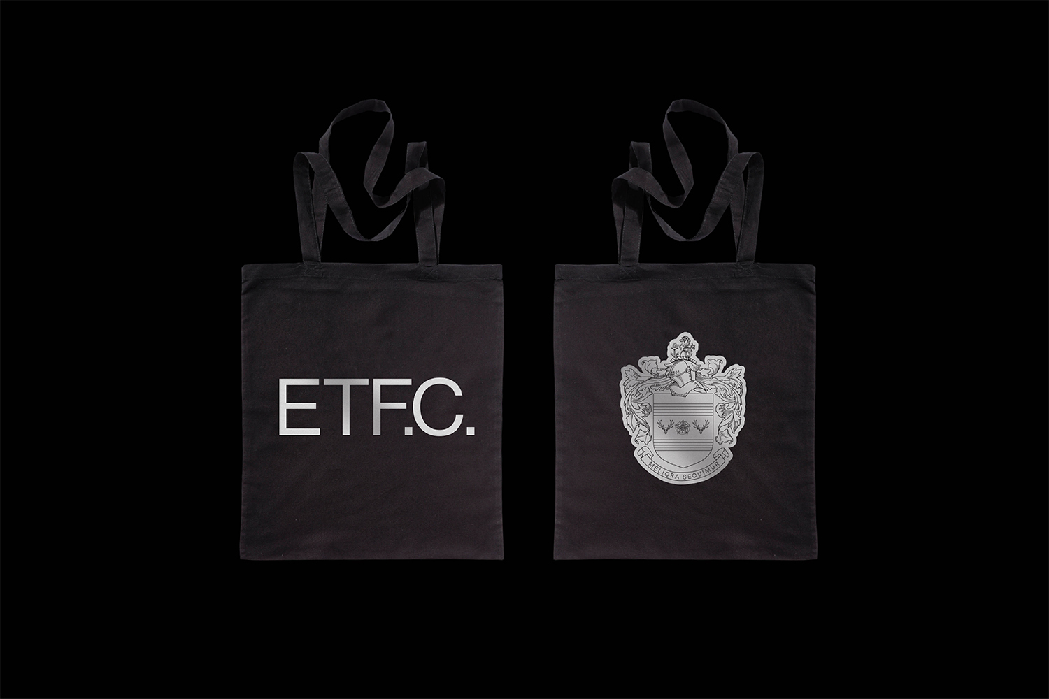 Two black tote bags displayed against a solid dark background, featuring silver printed branding on each side.