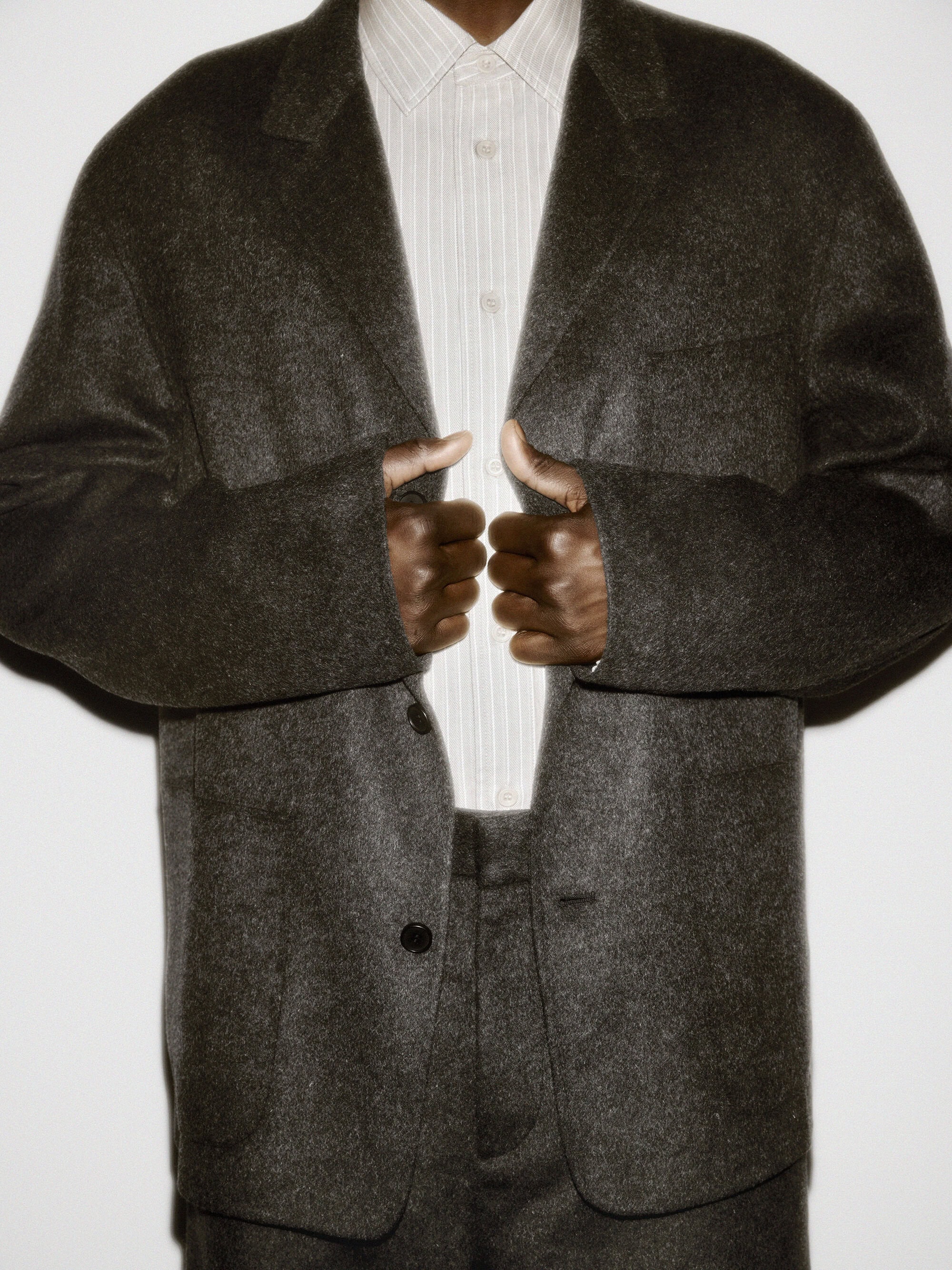 Person wearing a dark textured wool blazer and a striped button-down shirt against a plain white studio background.