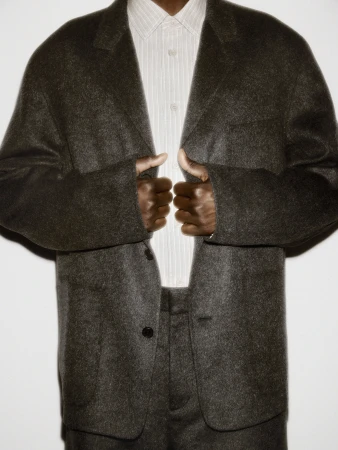 Person wearing a dark textured wool blazer and a striped button-down shirt against a plain white studio background.