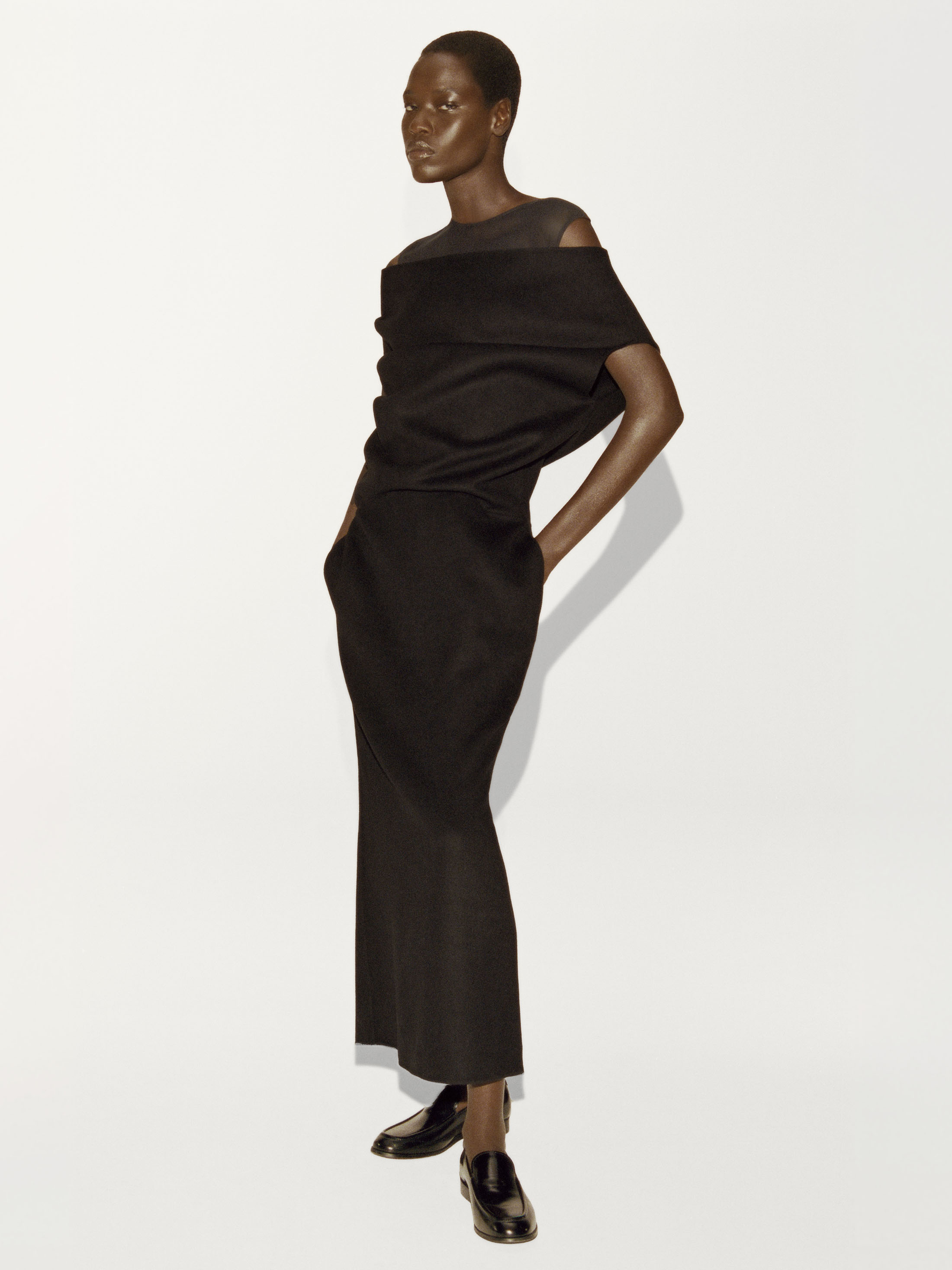 Model wearing a black draped top and matching long skirt against a white background