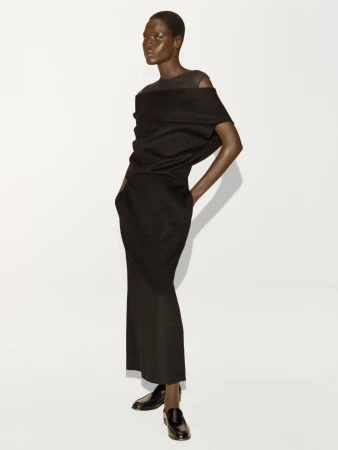 Model wearing a black draped top and matching long skirt against a white background