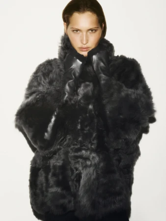 Model in a textured dark coat pulling the high collar up, captured against a clean white background for the COS ad campaign