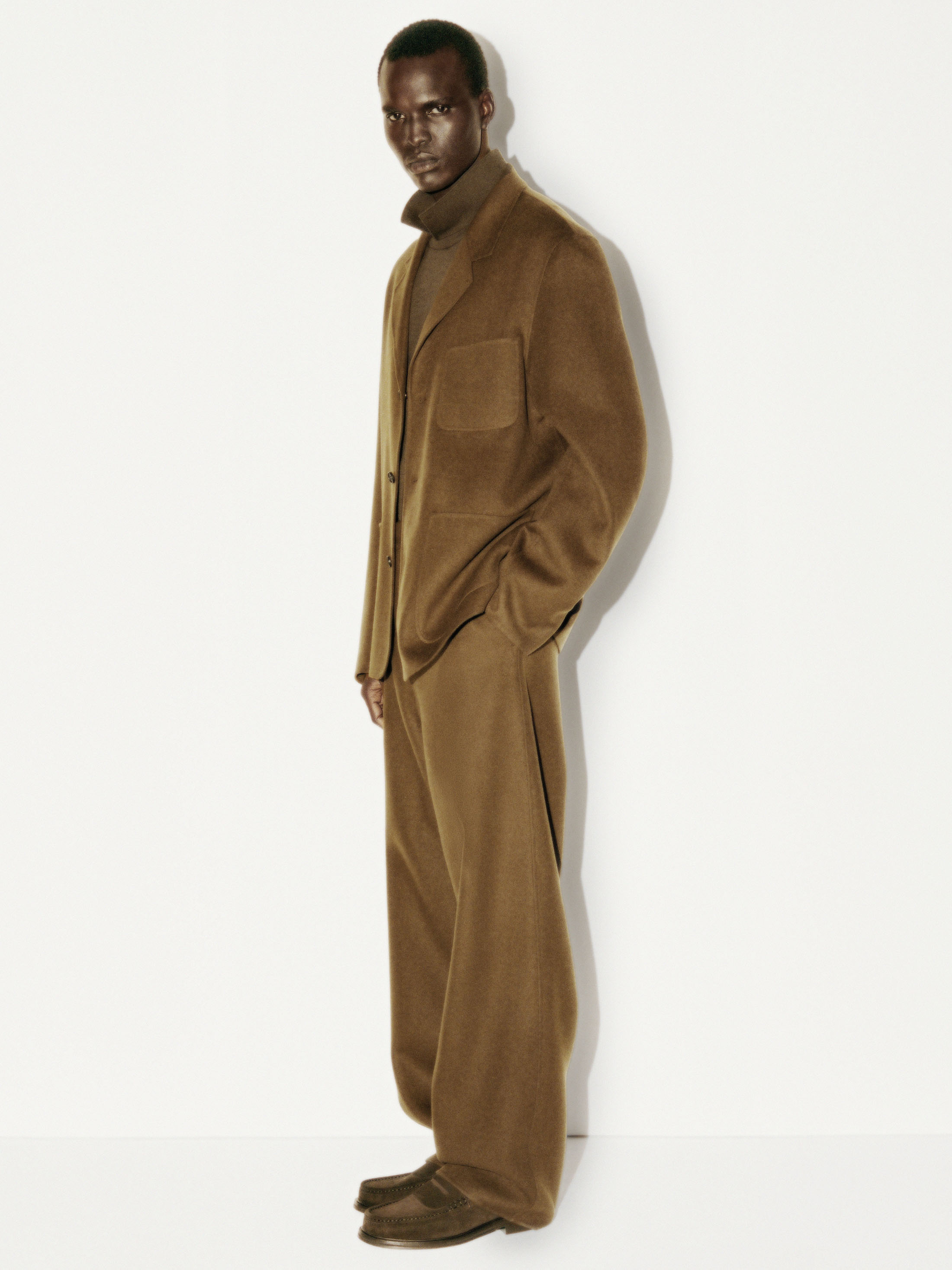 Man wearing a brown wool blazer and matching trousers standing against a white seamless background