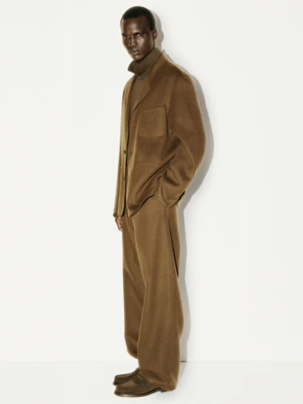 Man wearing a brown wool blazer and matching trousers standing against a white seamless background