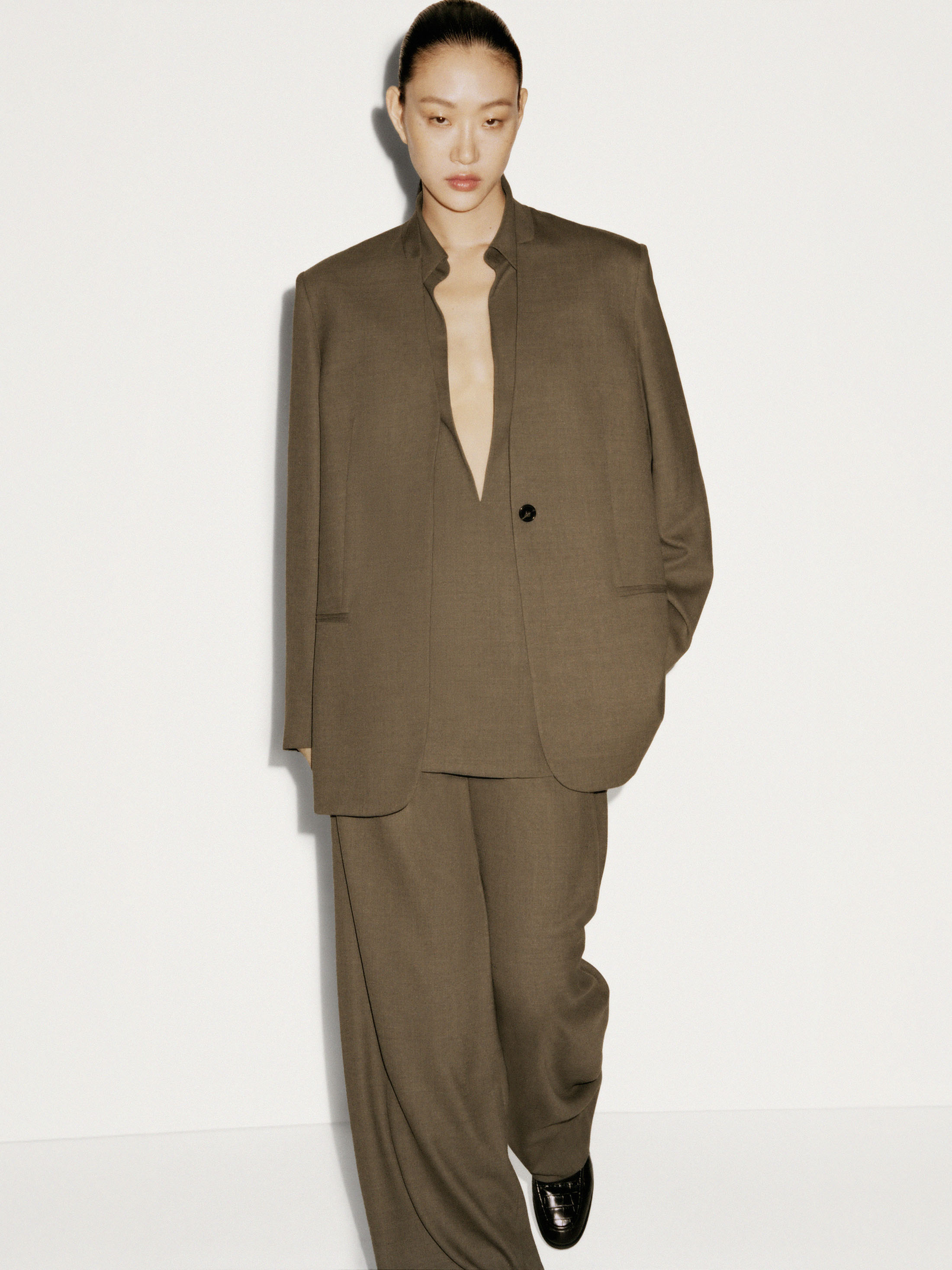 Model wearing a structured brown suit jacket and matching trousers against a plain white studio background.