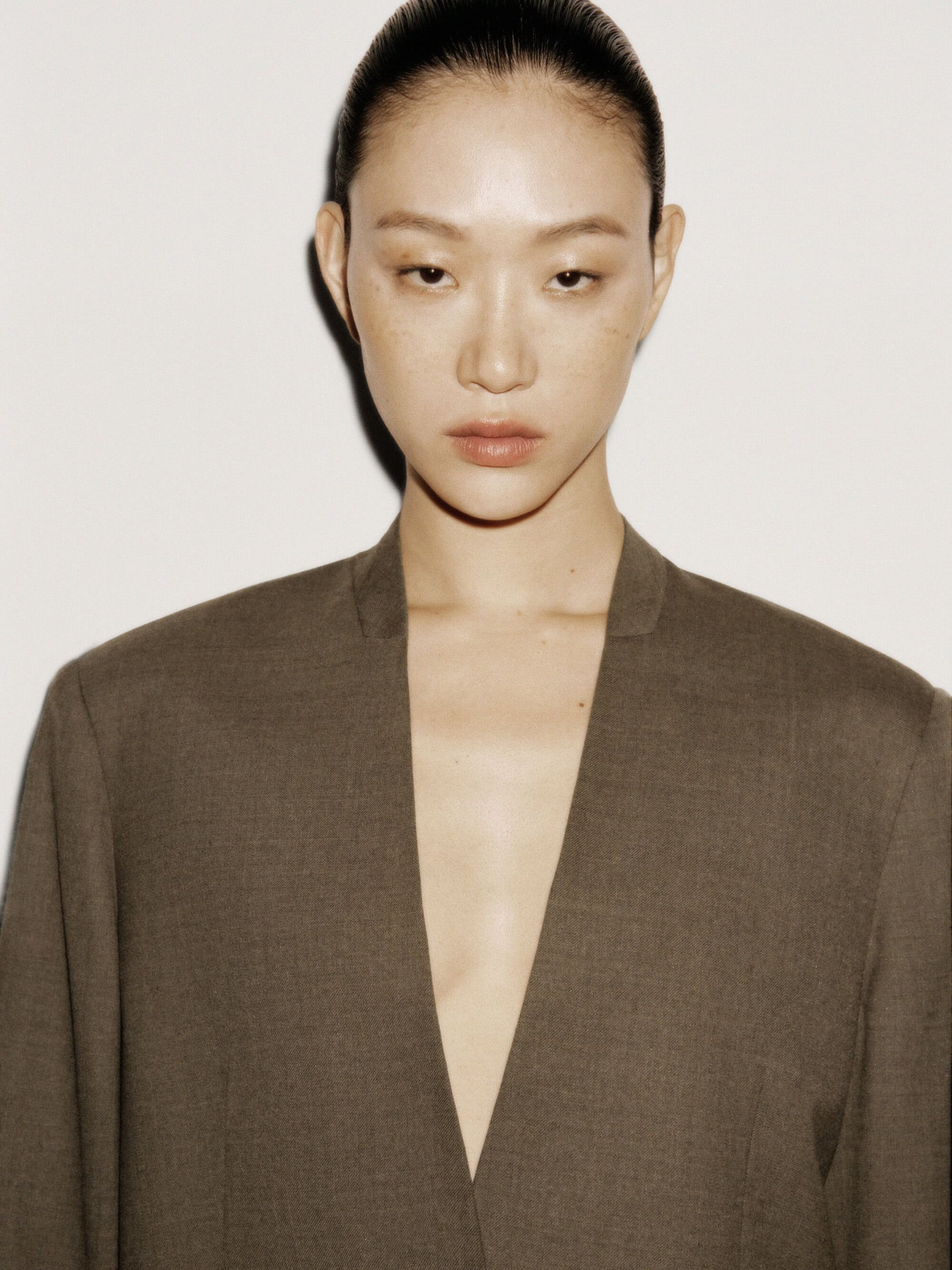 Model with slicked-back hair wearing a dark structured V-neck jacket against a neutral white background for COS