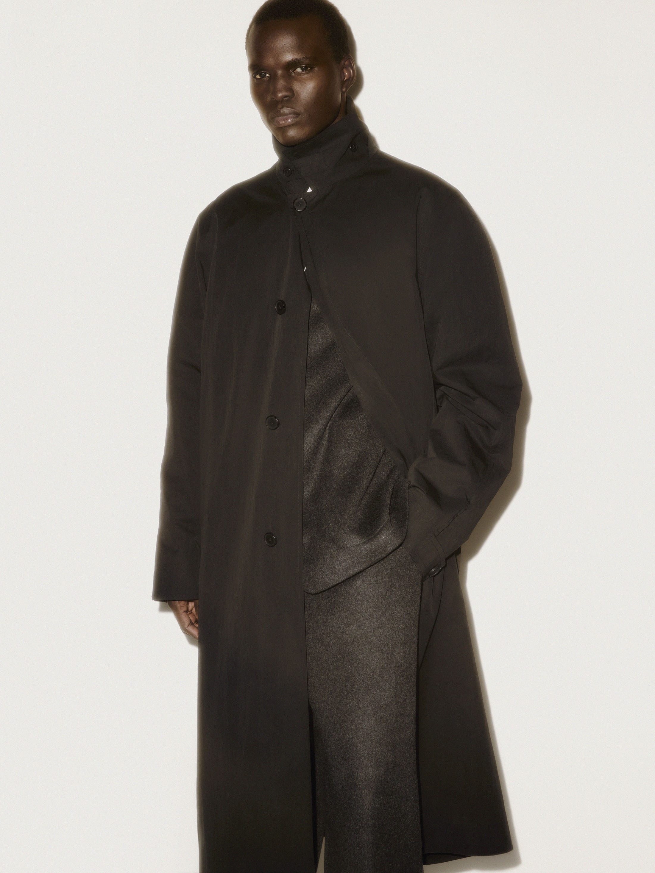 Black man wearing a dark buttoned overcoat against a plain light studio background
