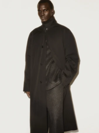 Black man wearing a dark buttoned overcoat against a plain light studio background