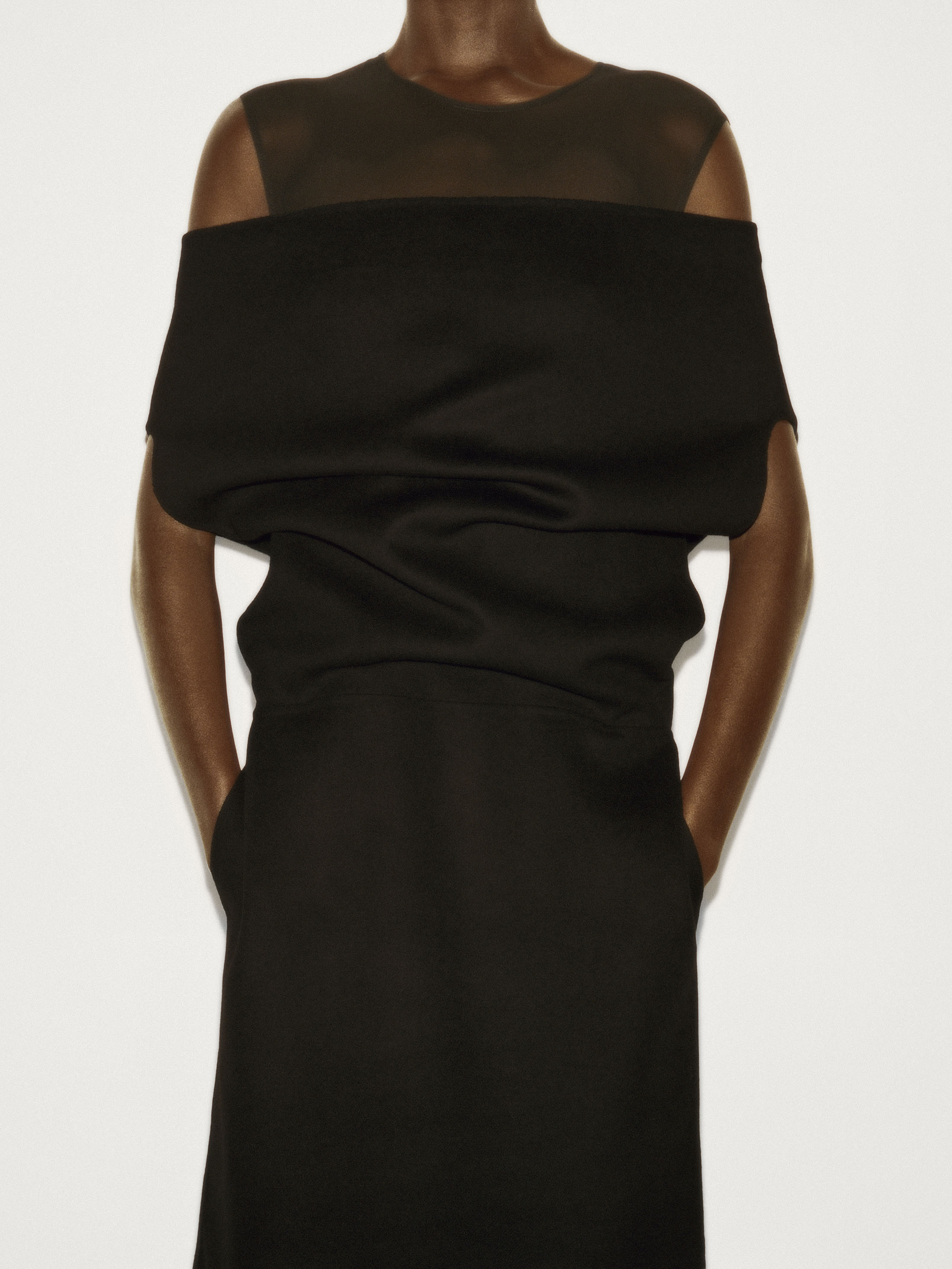 Model wearing a structured black dress against a plain off-white studio background for the COS Fall 2025 campaign.
