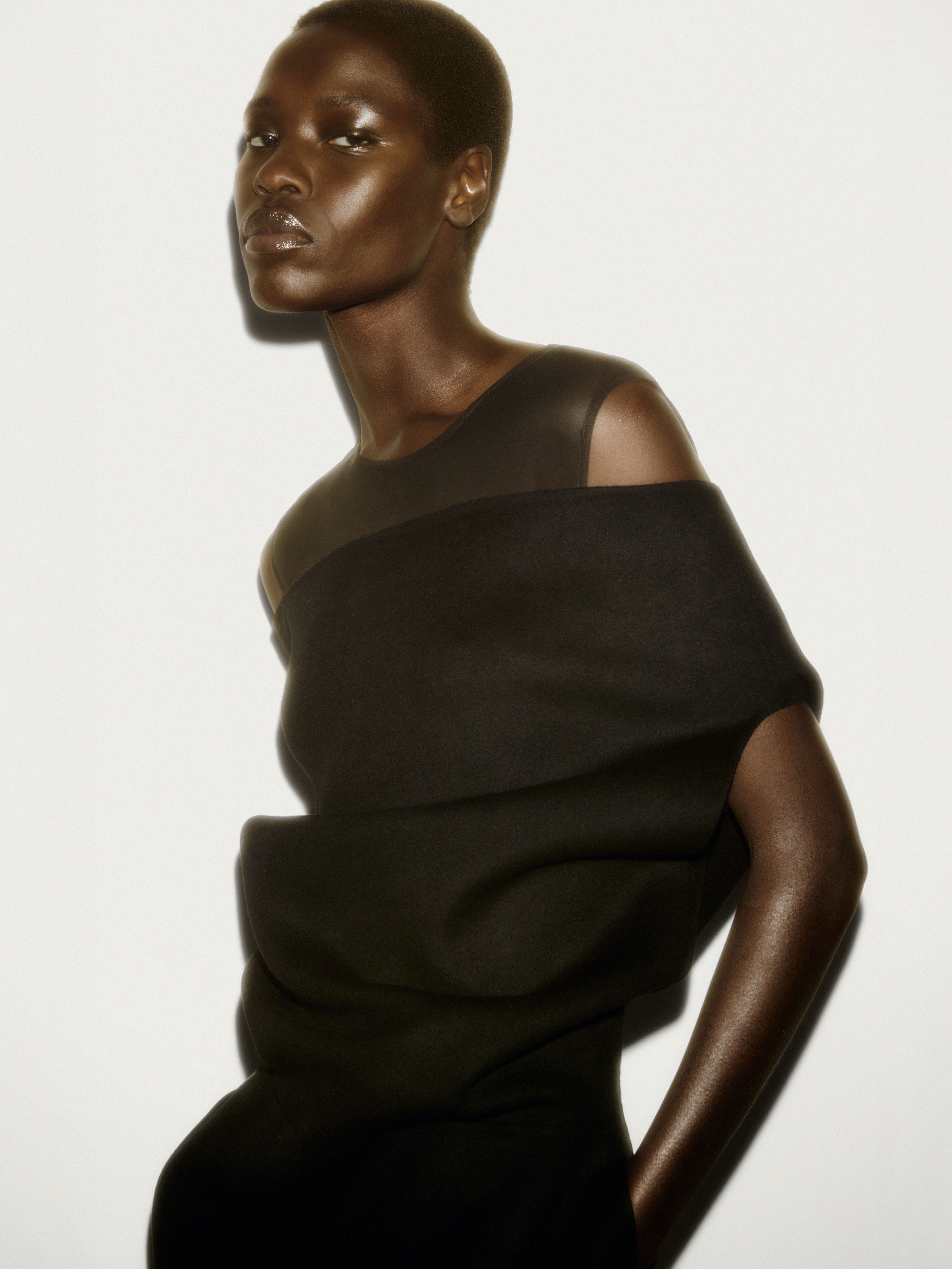 Model with short hair wearing a dark sculptural top against a bright white studio background for COS