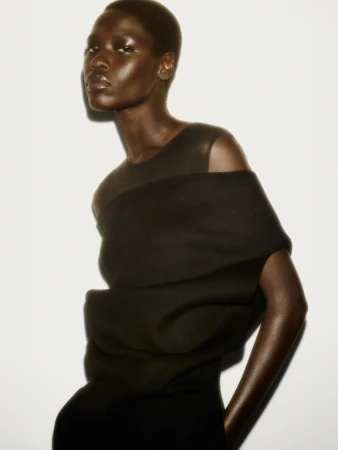 Model with short hair wearing a dark sculptural top against a bright white studio background for COS