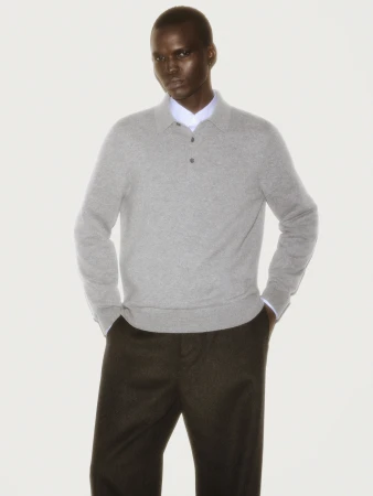 Man wearing a grey polo sweater and dark trousers against a white background for a COS ad campaign