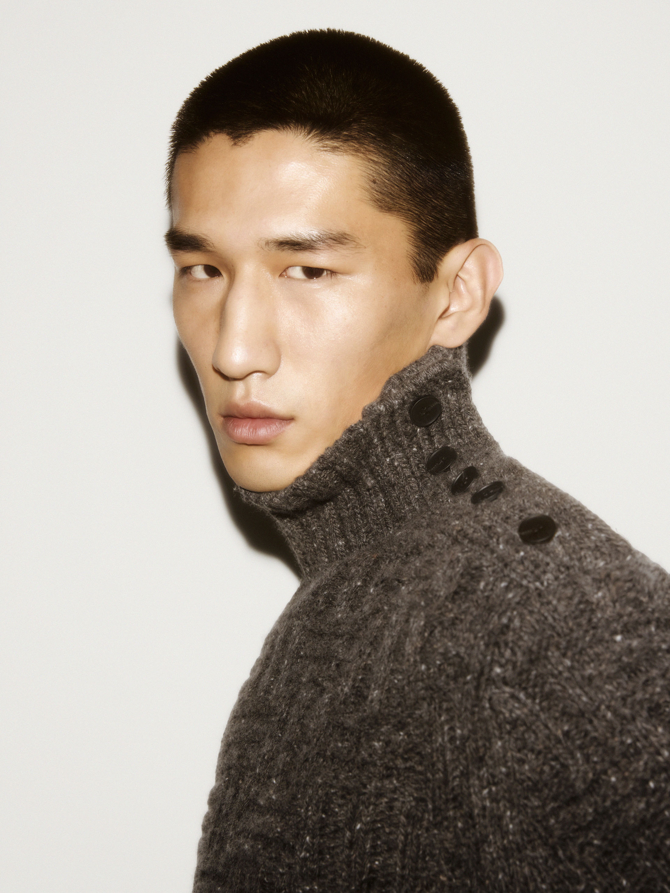 Close-up portrait of a man wearing a grey turtleneck sweater against a plain white background for the COS ad campaign.