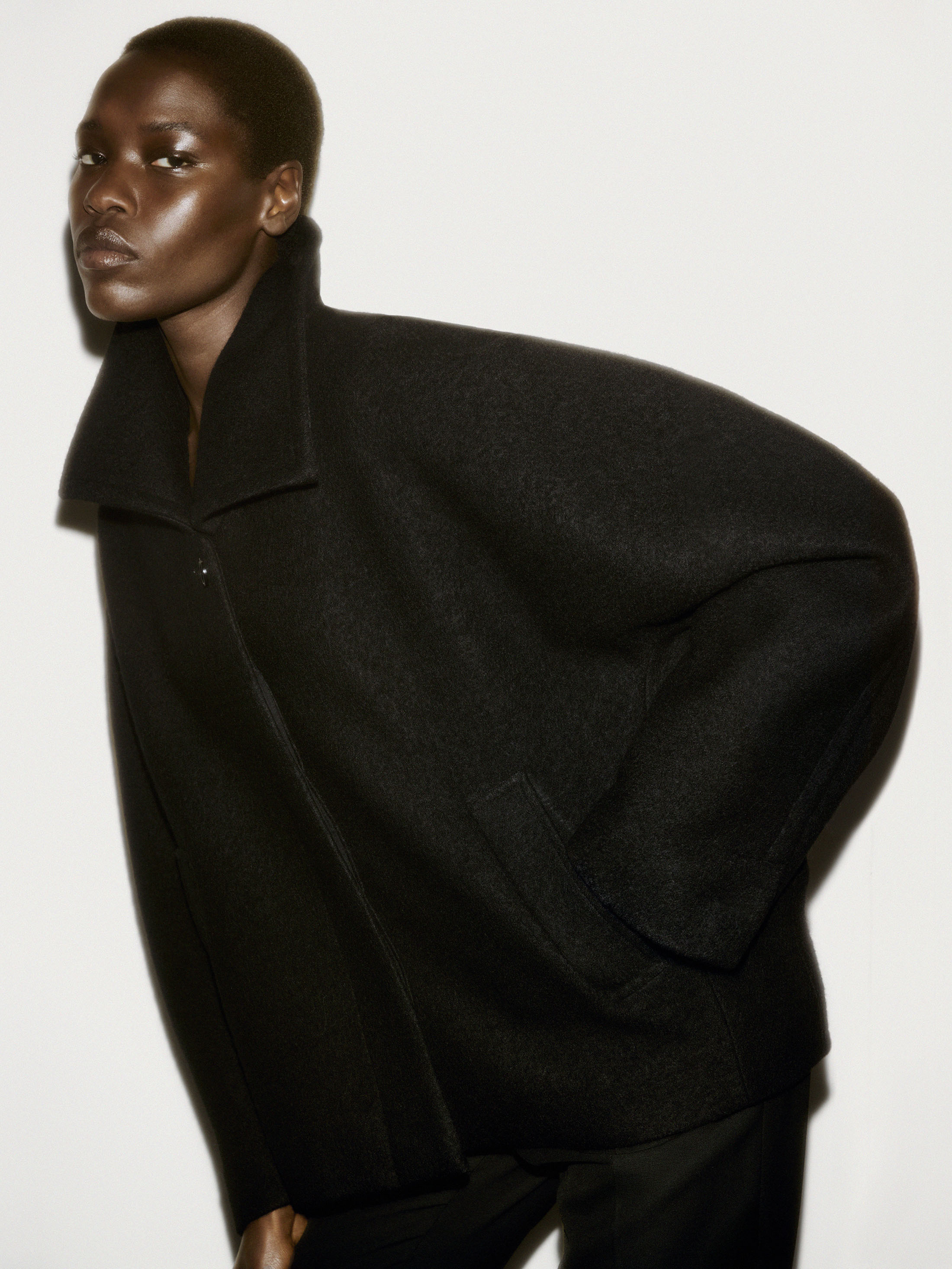 Model in a black structured wool coat against a plain white studio background