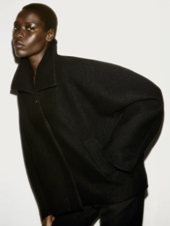 Model in a black structured wool coat against a plain white studio background