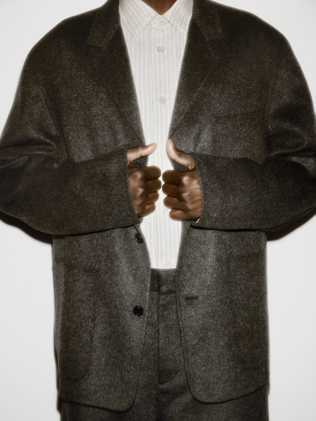 Person wearing a dark textured wool blazer and a striped button-down shirt against a plain white studio background.