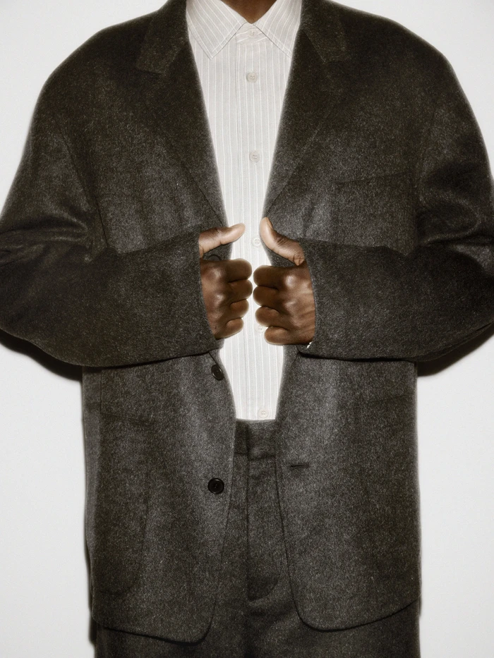 Person wearing a dark textured wool blazer and a striped button-down shirt against a plain white studio background.