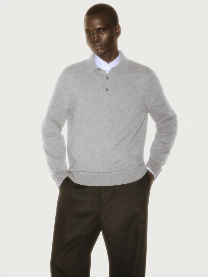 Man wearing a grey polo sweater and dark trousers against a white background for a COS ad campaign