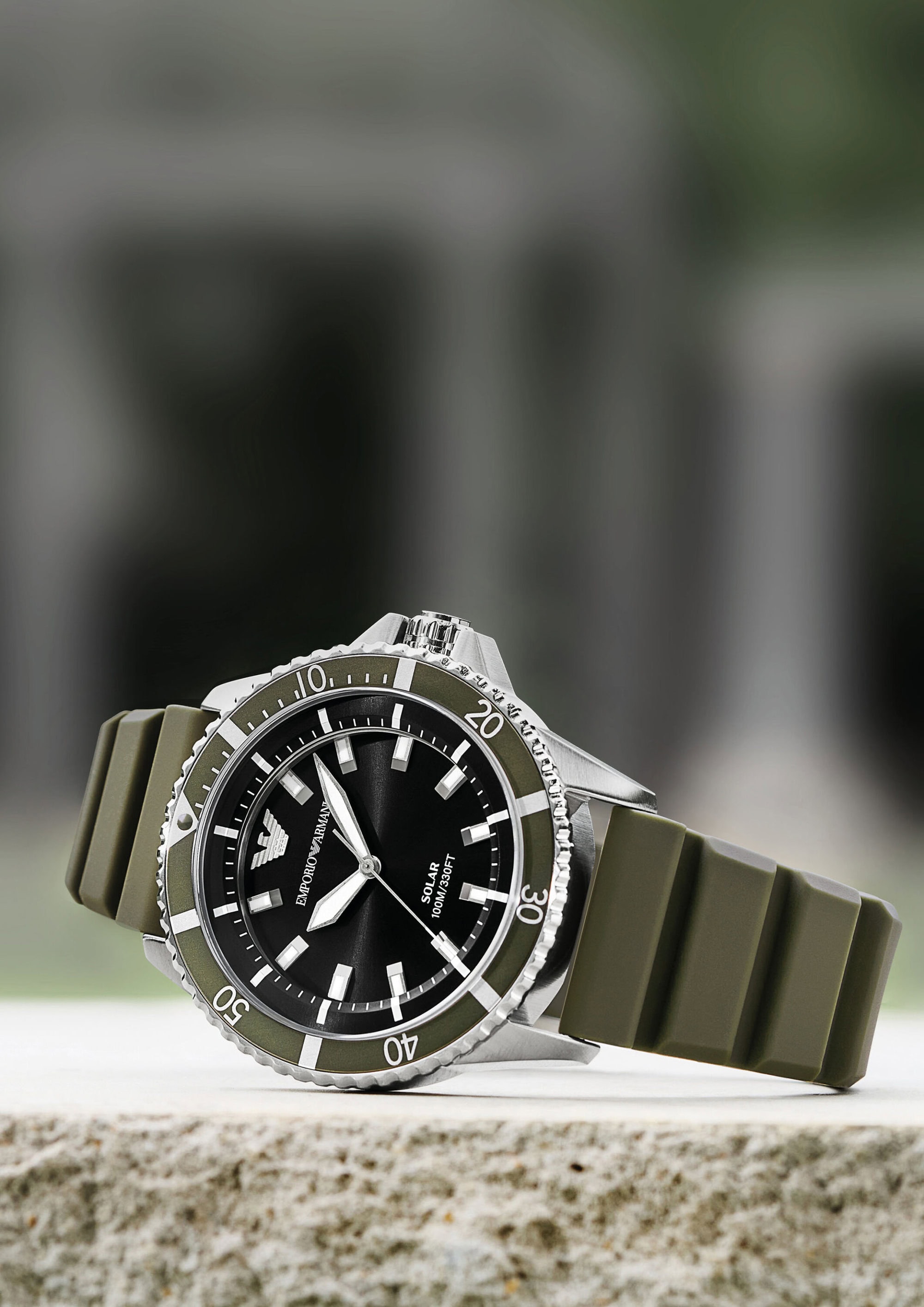 Emporio Armani green rubber strap watch resting on a light stone surface with a blurred architectural backdrop.