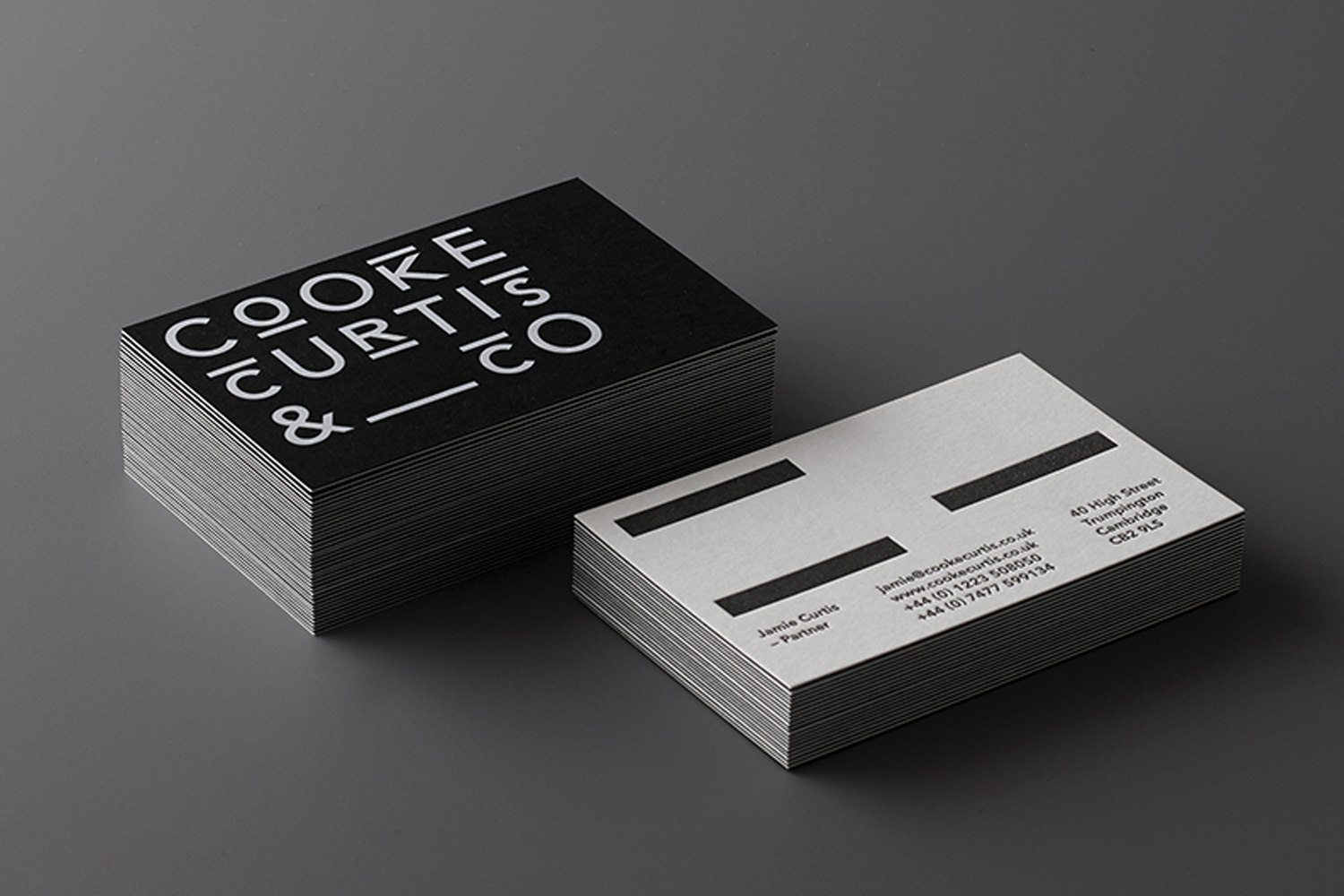 Two stacks of business cards for Cooke Curtis and Co on a dark grey surface, showing black and white minimalist typography.