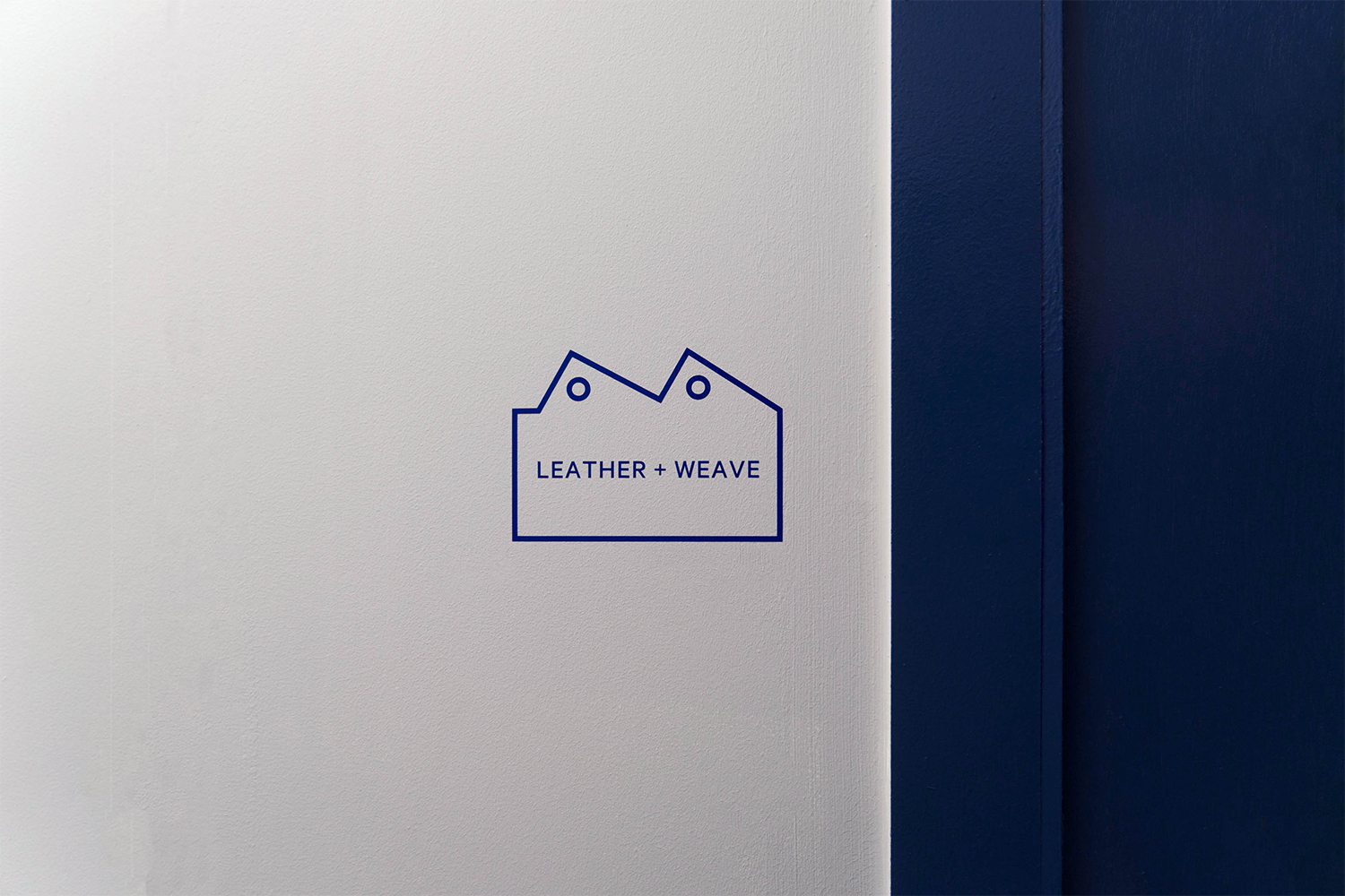 Blue graphic logo reading LEATHER + WEAVE on a white wall next to a dark blue vertical frame.
