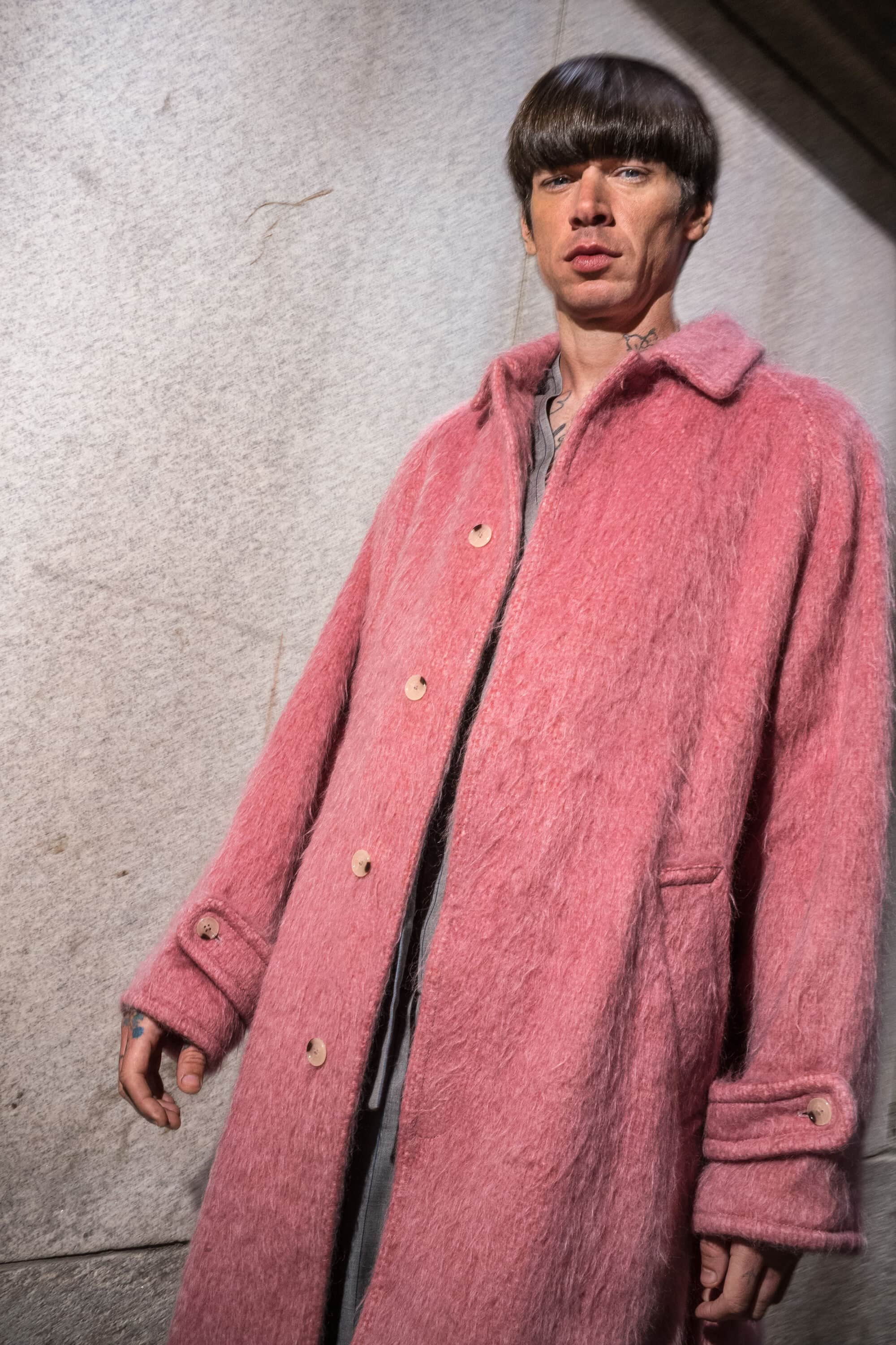 Model wearing a textured pink coat against a stone wall for Kenzo Fall 2025 campaign photographed by Bruce Gilden.