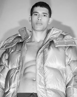 Monochrome portrait of a male model wearing an open puffer jacket against a plain light studio background.
