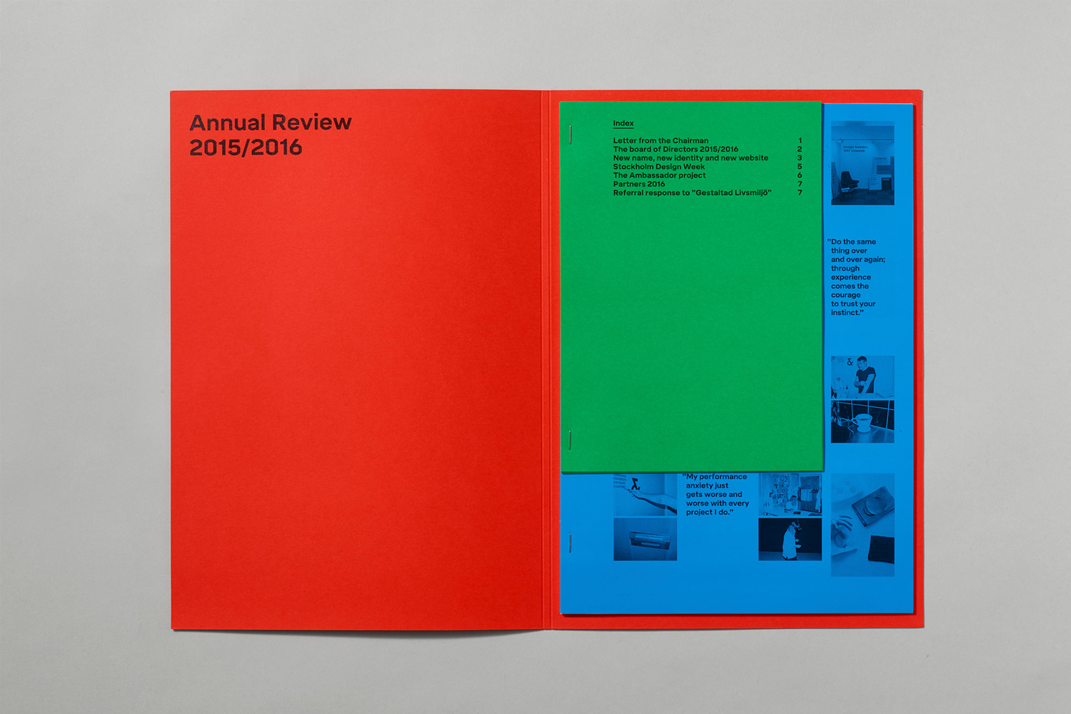 Open red folder containing a green booklet and blue pages against a neutral grey background surface.