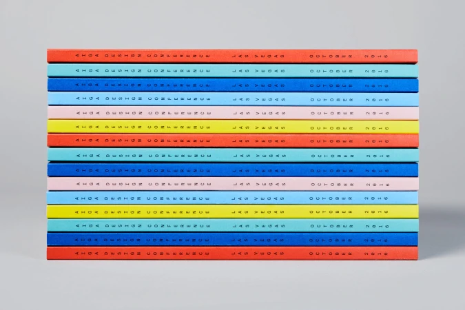 A stacked pile of colourful books featuring typographic text on the spines against a light grey studio background.