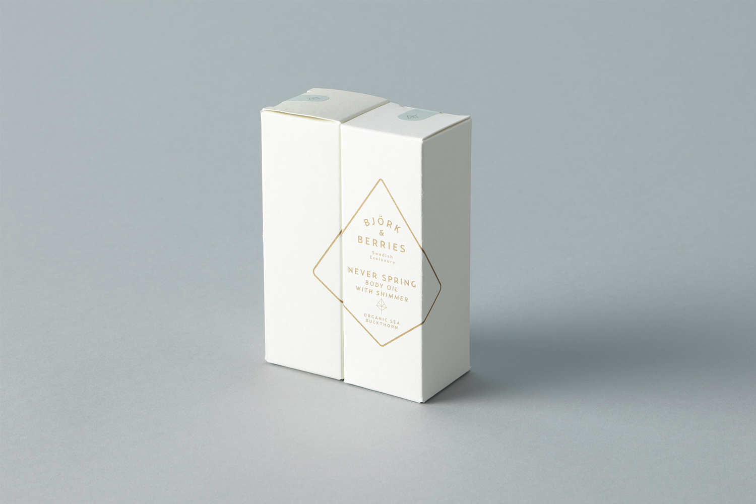 Two white rectangular product boxes with gold logo printing set against a solid grey seamless background.