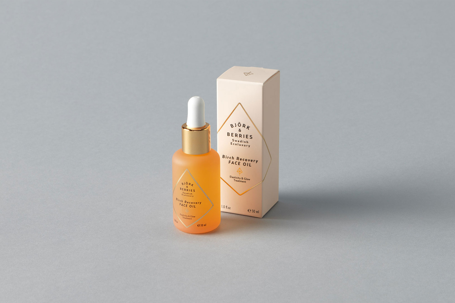 Bjork and Berries face oil dropper bottle next to its matching paper box on a grey seamless studio backdrop.