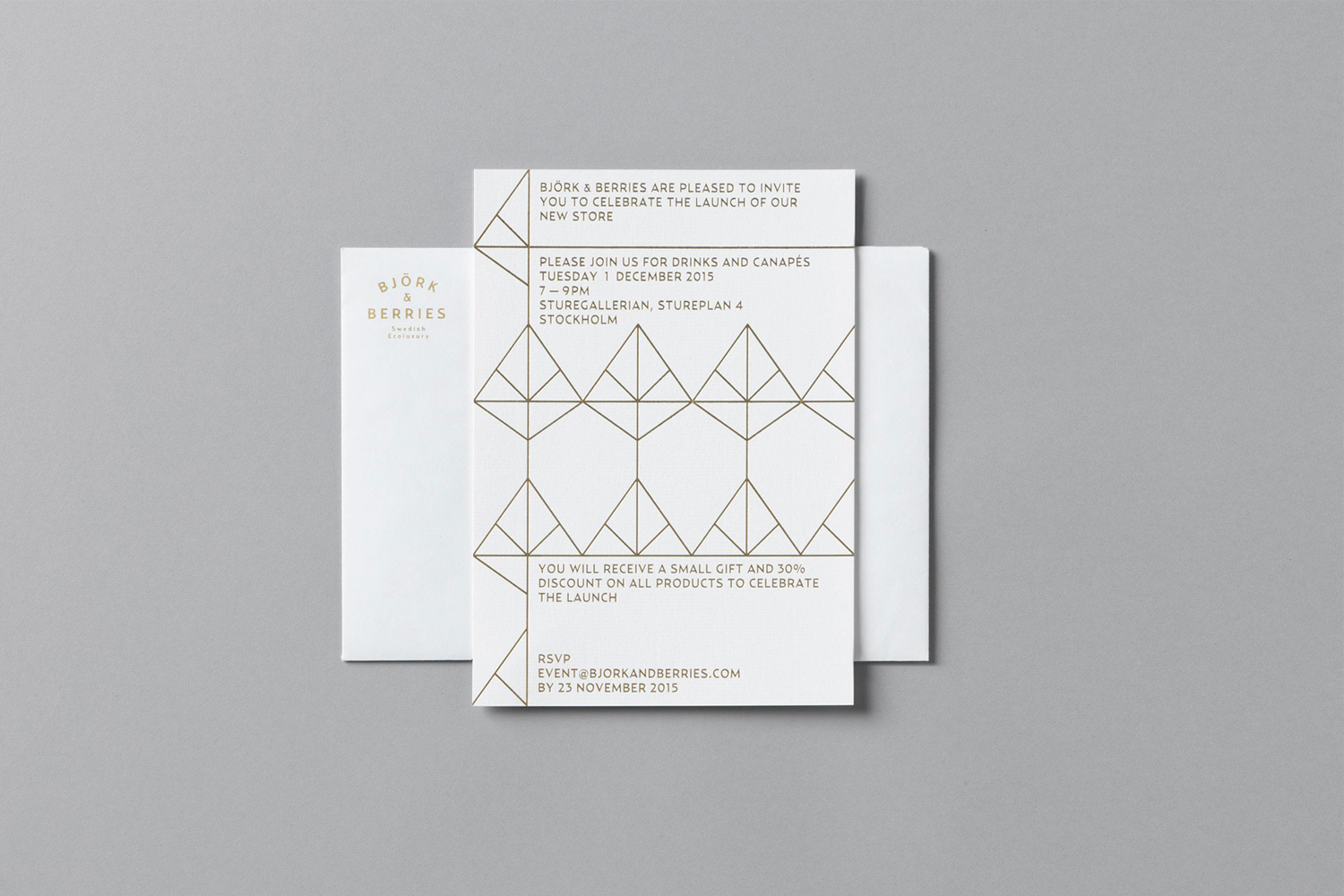 White store opening invitation card with geometric gold lines resting on a matching white envelope against a grey surface