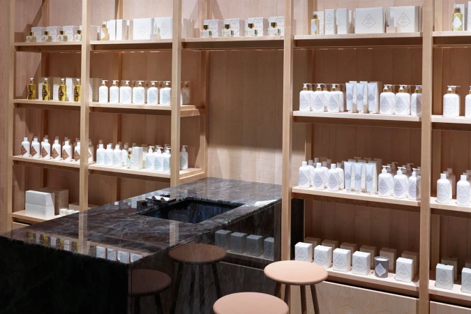 Wooden retail shelves lined with white product bottles and boxes above a polished dark marble counter with stools