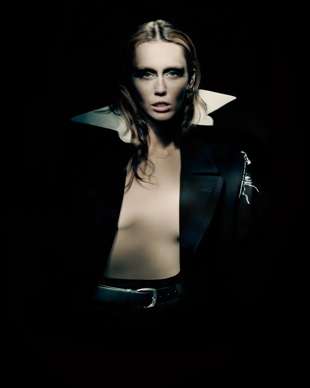 Miley Cyrus wearing a dark blazer with a large white collar against a dark background for Maison Margiela Fall 2025 ad campaign.