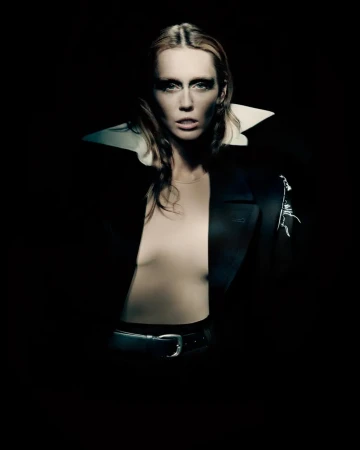 Miley Cyrus wearing a dark blazer with a large white collar against a dark background for Maison Margiela Fall 2025 ad campaign.
