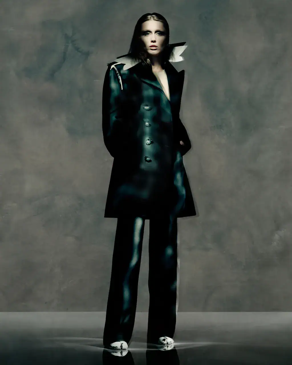 Model Miley Cyrus in dark apparel wearing a structured coat against a muted grey background for Maison Margiela Fall 2025 campaign.