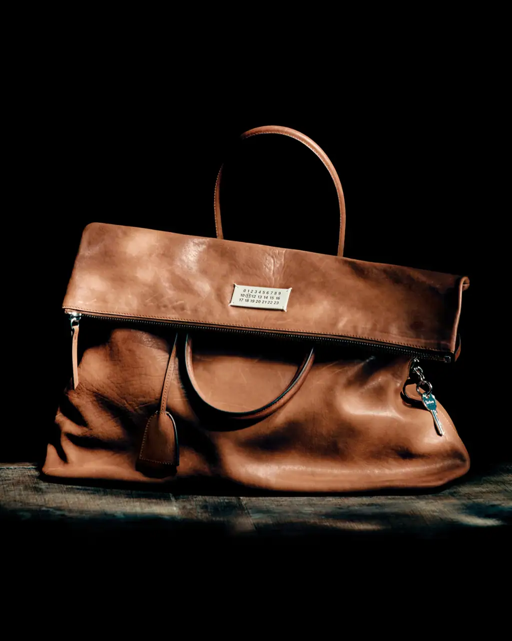 Tan leather Maison Margiela handbag resting on a dark surface against a deep black background