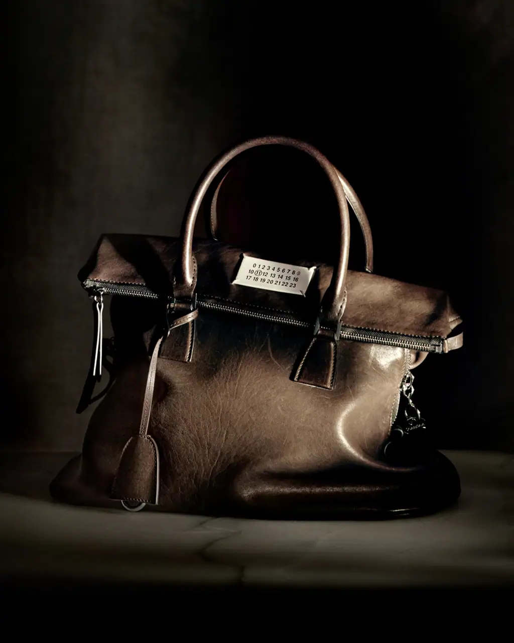 Maison Margiela brown leather handbag resting on a dark surface with atmospheric lighting.