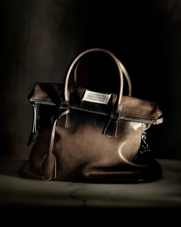 Maison Margiela brown leather handbag resting on a dark surface with atmospheric lighting.