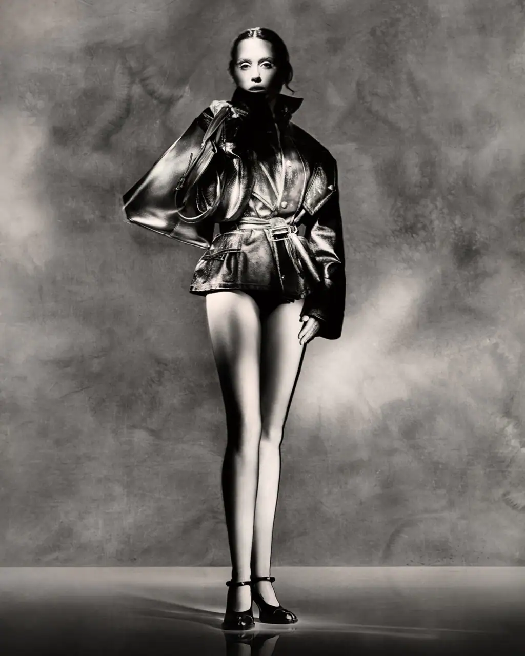 Miley Cyrus in a Maison Margiela ad campaign wearing a leather jacket and holding a bag against a textured background