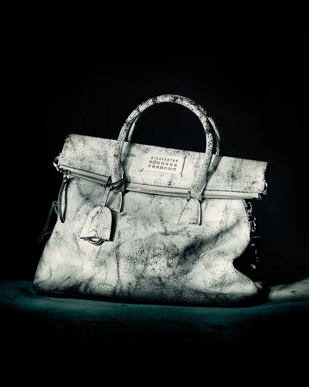 Distressed white leather handbag with top handles and numerical label against dark moody background
