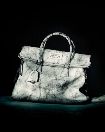 Distressed white leather handbag with top handles and numerical label against dark moody background