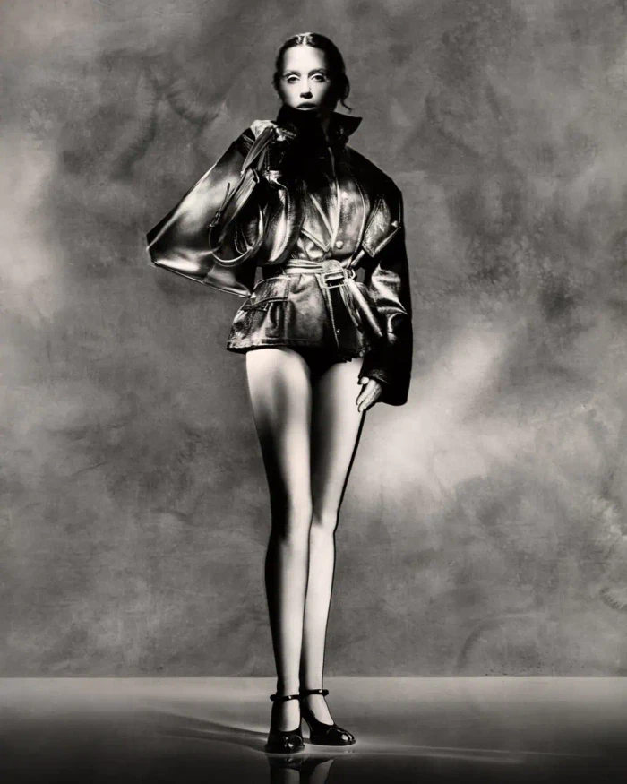 Miley Cyrus in a Maison Margiela ad campaign wearing a leather jacket and holding a bag against a textured background