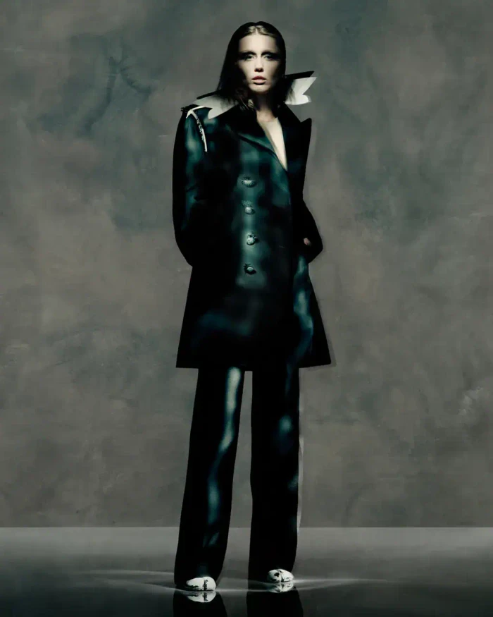 Model Miley Cyrus in dark apparel wearing a structured coat against a muted grey background for Maison Margiela Fall 2025 campaign.