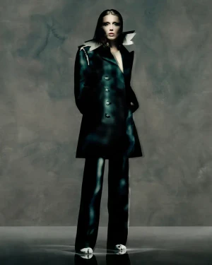 Model Miley Cyrus in dark apparel wearing a structured coat against a muted grey background for Maison Margiela Fall 2025 campaign.